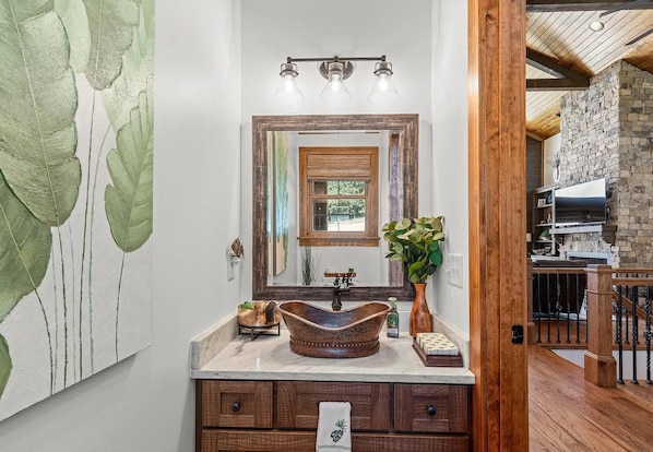 A bathroom with a large mirror, wooden vanity, and a stone wall.