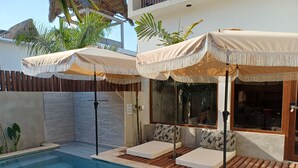 Un área junto a la piscina con sillones de descanso y sombrillas, una terraza de madera y vistas a la piscina.