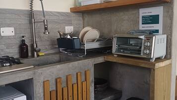 A compact kitchen with a built-in dishwasher, a toaster, and wooden shelves above the counter.