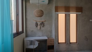 Una habitación con un escritorio blanco, una silla, un atrapasueños colgante y una ventana con persianas.