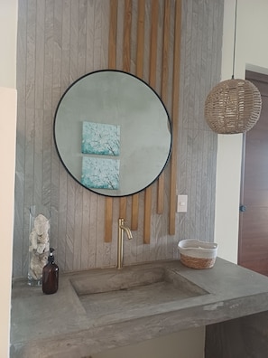 A bathroom with a large mirror, a wooden panel wall, a sink, a soap dispenser, and a woven basket. - Areia Bali: A/C, private pool, just steps from the ocean (El Paredón Buena Vista)