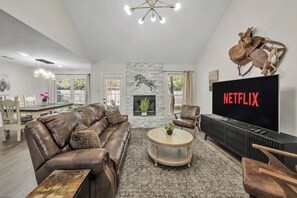 A modern living room with a leather sofa, a coffee table, a fireplace, and a television displaying 'NETFLIX'. - Montana: Custom Home, 4 BR, Close to Texas A&M (College Station)