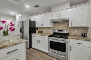 A modern kitchen with white cabinetry, stainless steel appliances, and a granite countertop. - Montana: Custom Home, 4 BR, Close to Texas A&M (College Station)
