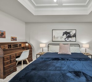 A bedroom with a large bed, a wooden dresser, a desk, and a chair. There are two bedside lamps and a framed picture on the wall. - Montana: Custom Home, 4 BR, Close to Texas A&M (College Station)