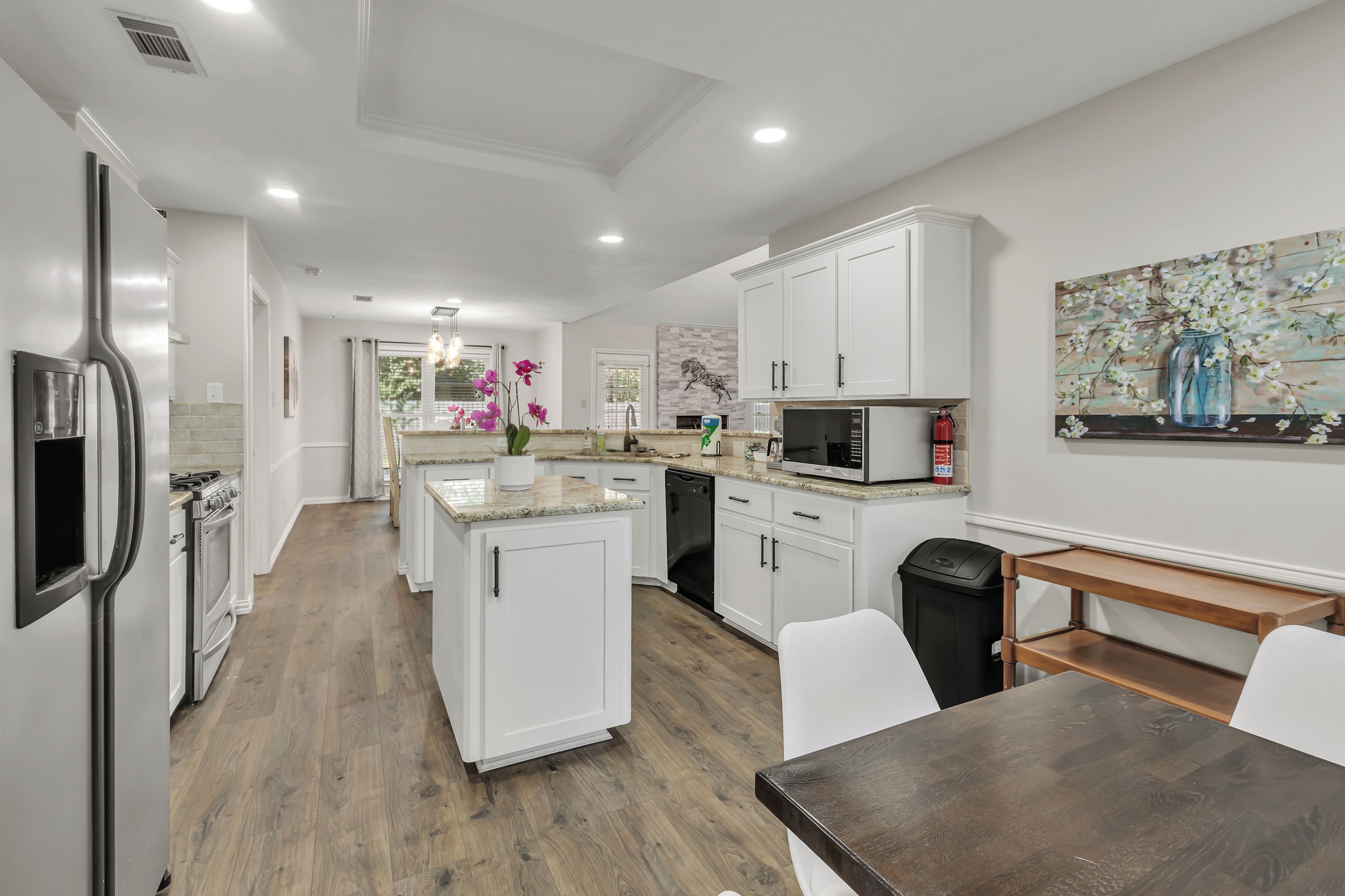 A modern kitchen with white cabinets, a built-in microwave, and a dining area with a wooden table and chairs.