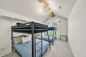 Une chambre de dortoir avec des lits superposés, un luminaire au plafond et une fenêtre avec des stores.