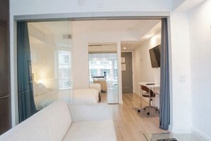 Une chambre d’hôtel moderne avec une paroi en verre, un canapé, un bureau et un téléviseur.