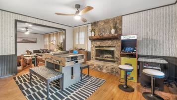 A modern living room with a foosball table, a fireplace, and a retro arcade machine.