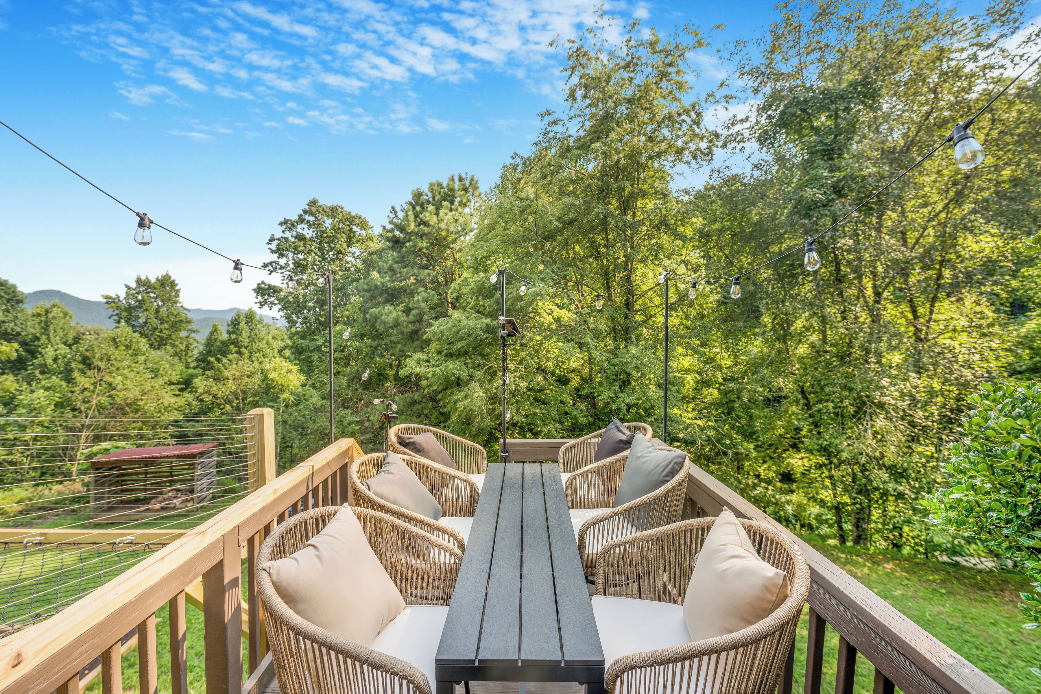 An outdoor deck with wicker furniture and a table, surrounded by trees and a clear sky.