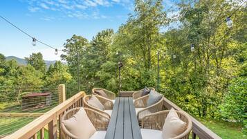 An outdoor deck with wicker furniture and a table, surrounded by trees and a clear sky.