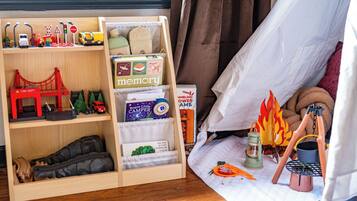 A child's play area with a wooden shelf containing toys and books.
