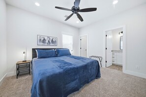 A bedroom with a bed, a ceiling fan, a nightstand, a lamp, a painting, and a bathroom with a mirror and cabinets. - Sterling-2 Min Drive to Texas A&M, Comfy King Beds (College Station)