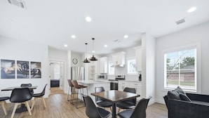 Une cuisine moderne avec des meubles blancs, un îlot central et un coin repas comprenant une table en bois et des chaises noires.
