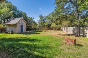 A small wooden shed with a door and windows, surrounded by a grassy yard with trees and a wooden fence. - Walton: 60 Second Drive to Texas A&M (College Station)