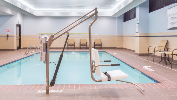 A swimming pool with a lift chair, chairs, and a sign on the wall. - Mobility Suite w/ Roll-In Shower | Free Breakfast (Seattle)