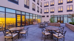 A modern hotel courtyard with outdoor seating, large windows, and a stone retaining wall. - Mobility Suite w/ Roll-In Shower | Free Breakfast (Seattle)
