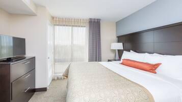 A hotel room with a bed, a TV on a dresser, a lamp, and a window with curtains.