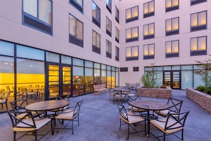 Une cour d’hôtel moderne dotée d’un espace extérieur aménagé avec des sièges, de grandes fenêtres et un mur de soutènement en pierre.