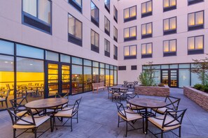 Une cour d’hôtel moderne dotée d’un espace extérieur aménagé avec des sièges, de grandes fenêtres et un mur de soutènement en pierre.