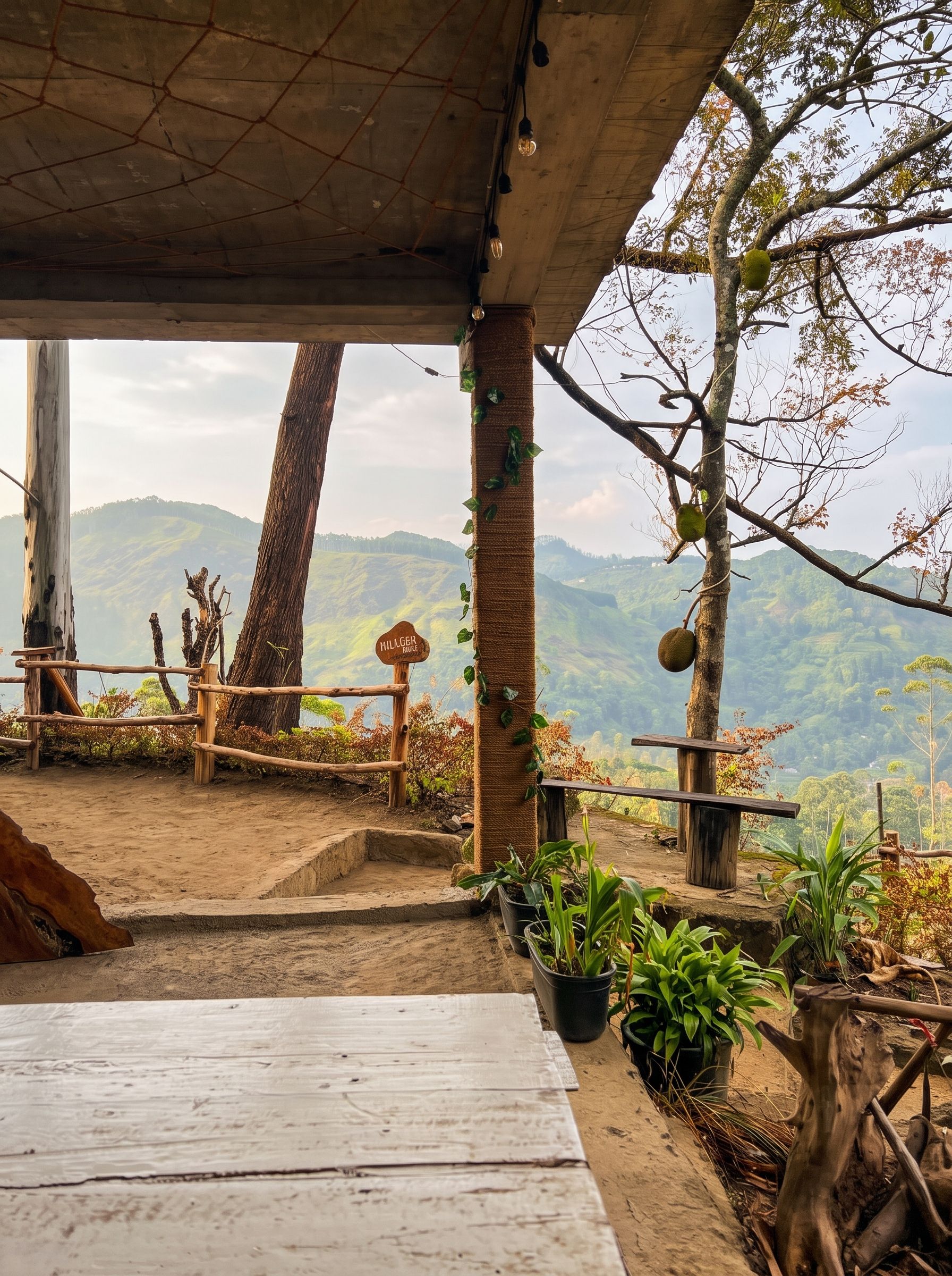 A rustic outdoor seating area with a wooden table and chairs, surrounded by plants and a view of a hilly landscape.