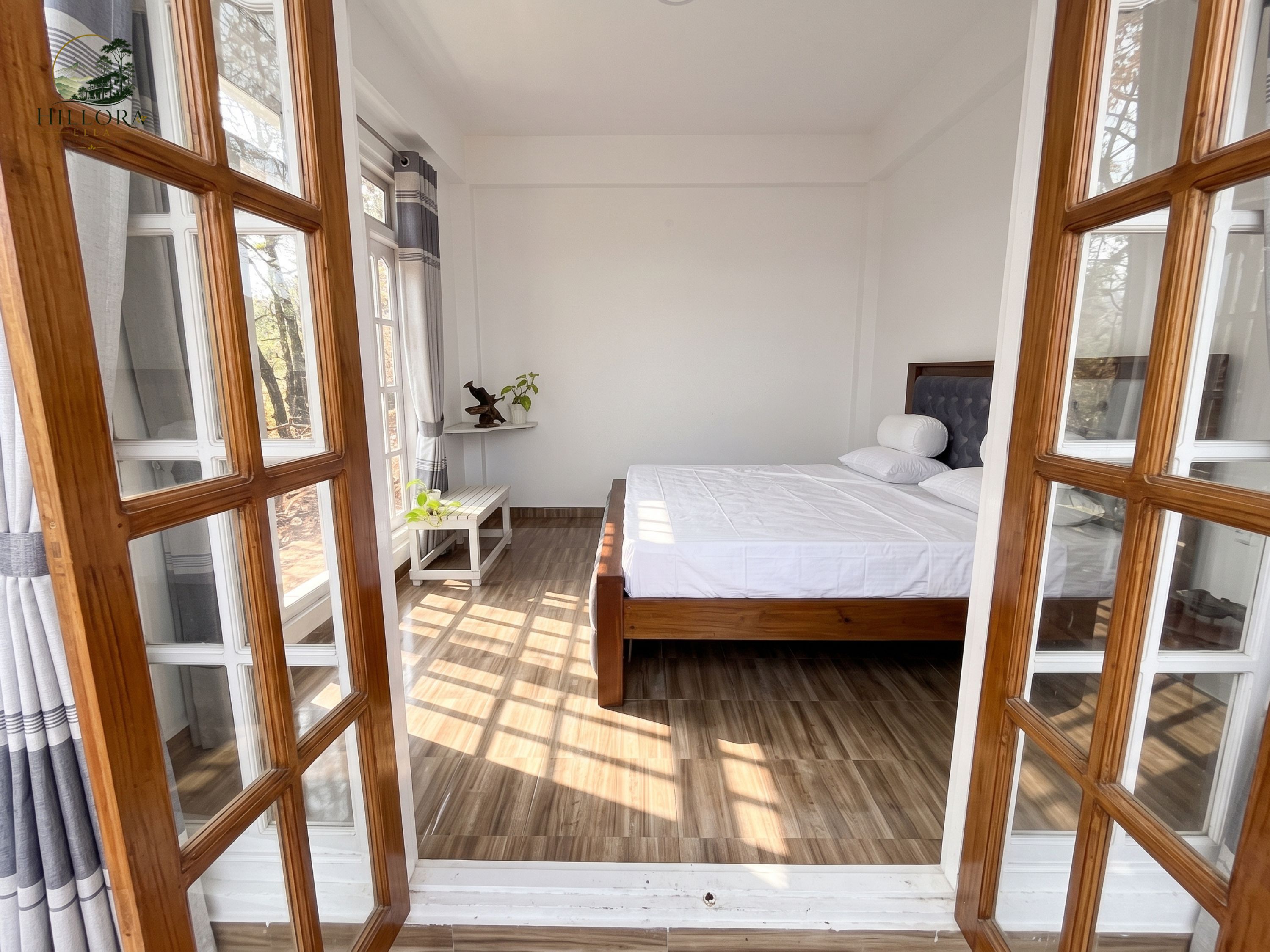 A bedroom with a bed, a nightstand, a shelf with decorative items, and a view through large windows.