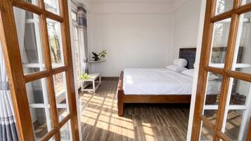 A bedroom with a bed, a nightstand, a shelf with decorative items, and a view through large windows.