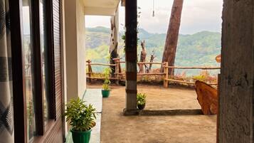Un balcón con vistas a un paisaje montañoso, plantas en macetas y una cerca de madera.