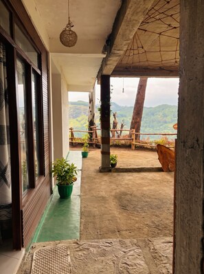 Un balcón con vistas a un paisaje montañoso, plantas en macetas y una cerca de madera.