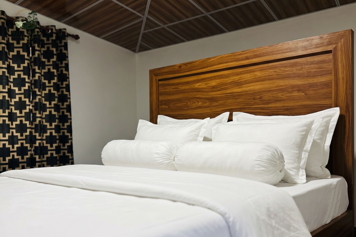 A bed with white bedding and a wooden headboard in a room with a patterned curtain.