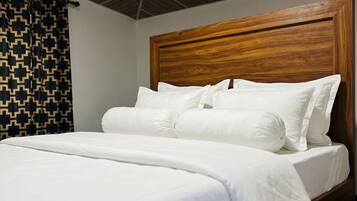 Una cama con ropa blanca y un cabecero de madera en una habitación con cortina estampada.