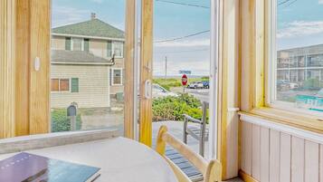 A room with a table and chairs, a window with a view of a street and houses, and a stop sign in the distance.