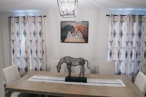 A dining area with a table, chairs, a decorative horse sculpture, patterned curtains, and a framed picture on the wall. - 7 BRs 3 BAs - 10 beds! (Groves)