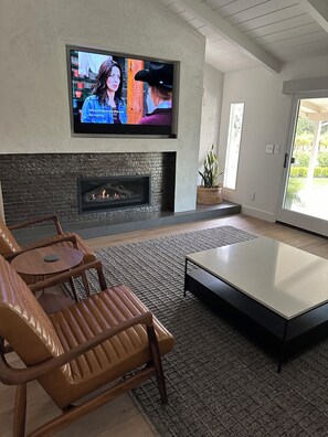 Ein modernes Wohnzimmer mit einem flachbildfernseher an der Wand, einem Kamin, Ledersofas und einem Couchtisch.