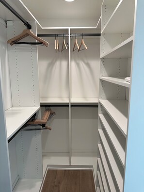 Ein begehbarer Kleiderschrank mit offenen Regalen, Holzhängern und einer spiegelnden Schranktür.