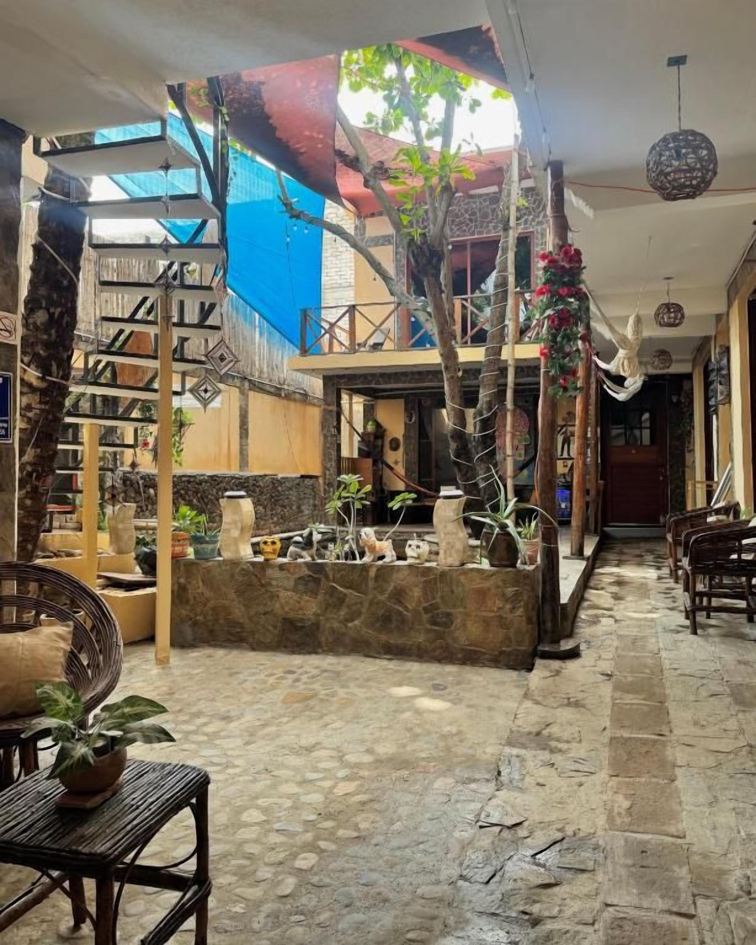 Un patio interior con suelo de piedra, una escalera y diferentes plantas y muebles.