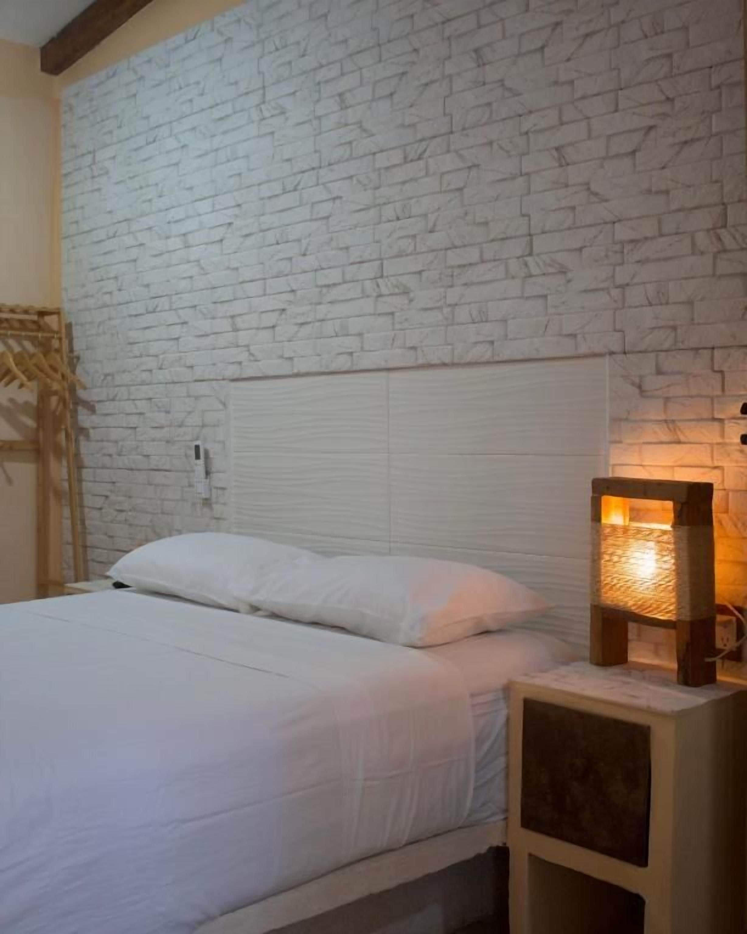 Una cama con ropa de cama blanca, un cabecero de madera y una mesita de noche con una lámpara.