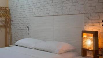 Una cama con ropa de cama blanca, un cabecero de madera y una mesita de noche con una lámpara.