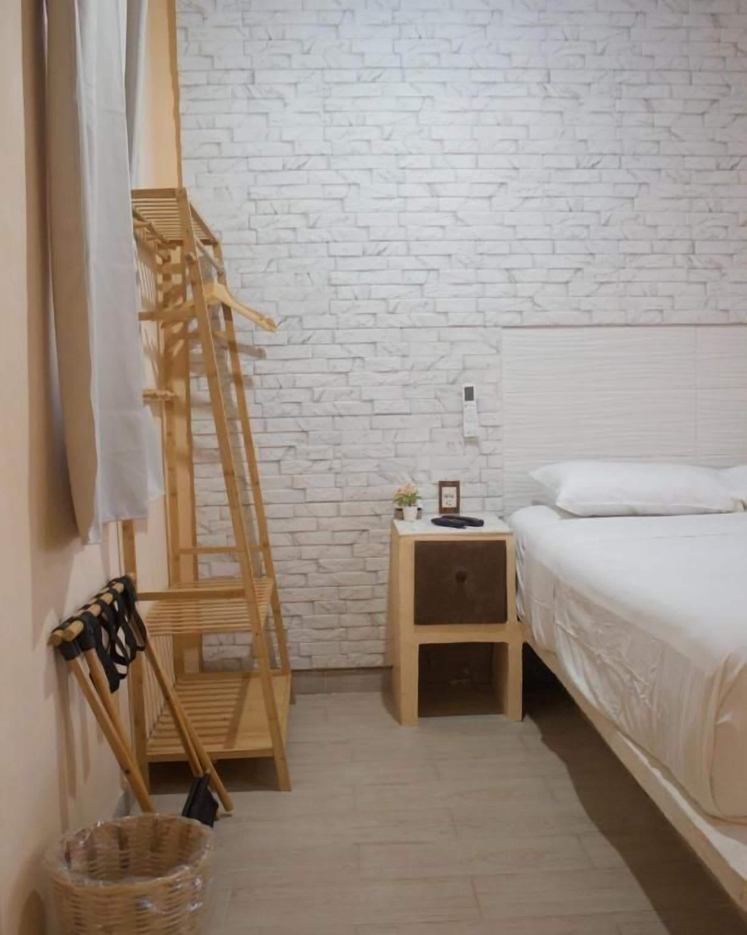 Un dormitorio con pared de ladrillo blanco, escalera de madera, mesita de noche con lámpara y cama con ropa blanca.