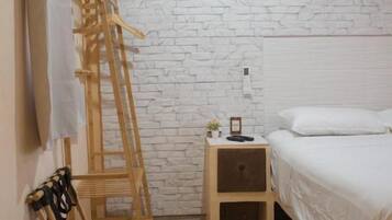 Un dormitorio con pared de ladrillo blanco, escalera de madera, mesita de noche con lámpara y cama con ropa blanca.