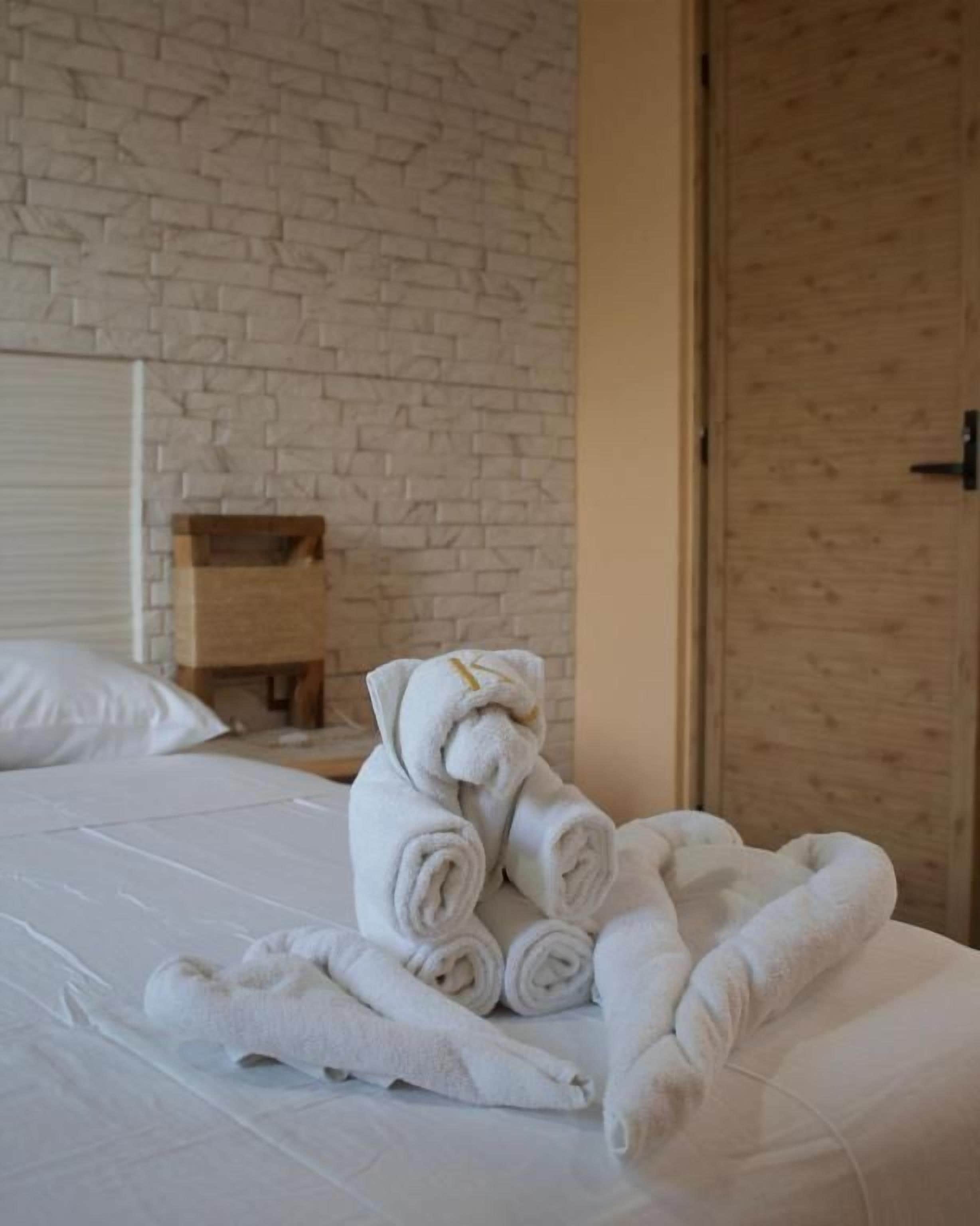 Une chambre d’hôtel avec un mur en briques blanches, une porte en bois et un lit sur lequel sont pliées des serviettes.