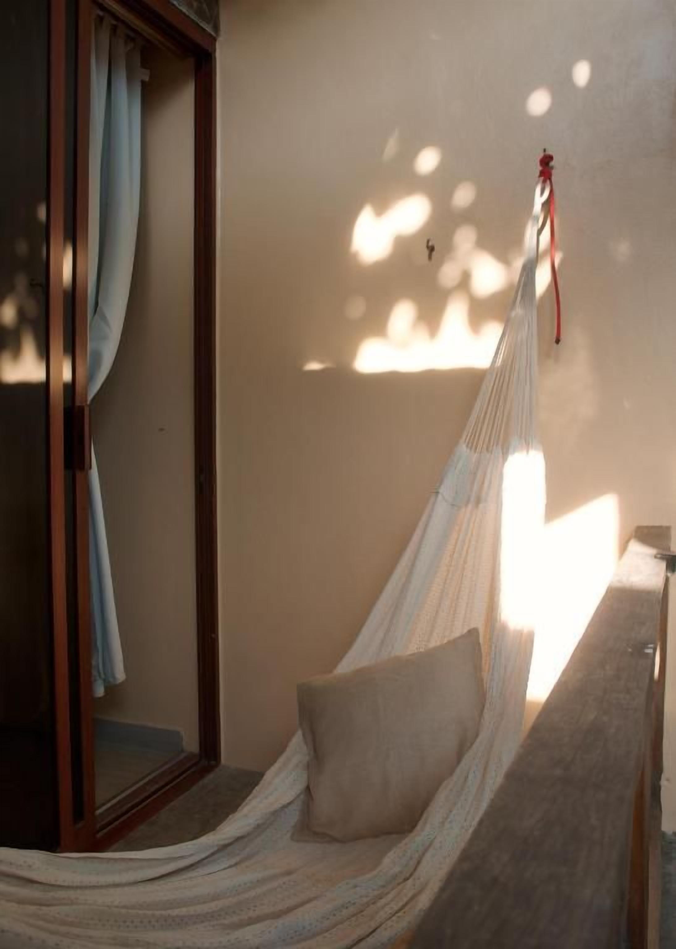 A hammock tied to a wooden structure, a window with curtains, and a wall with a light fixture.