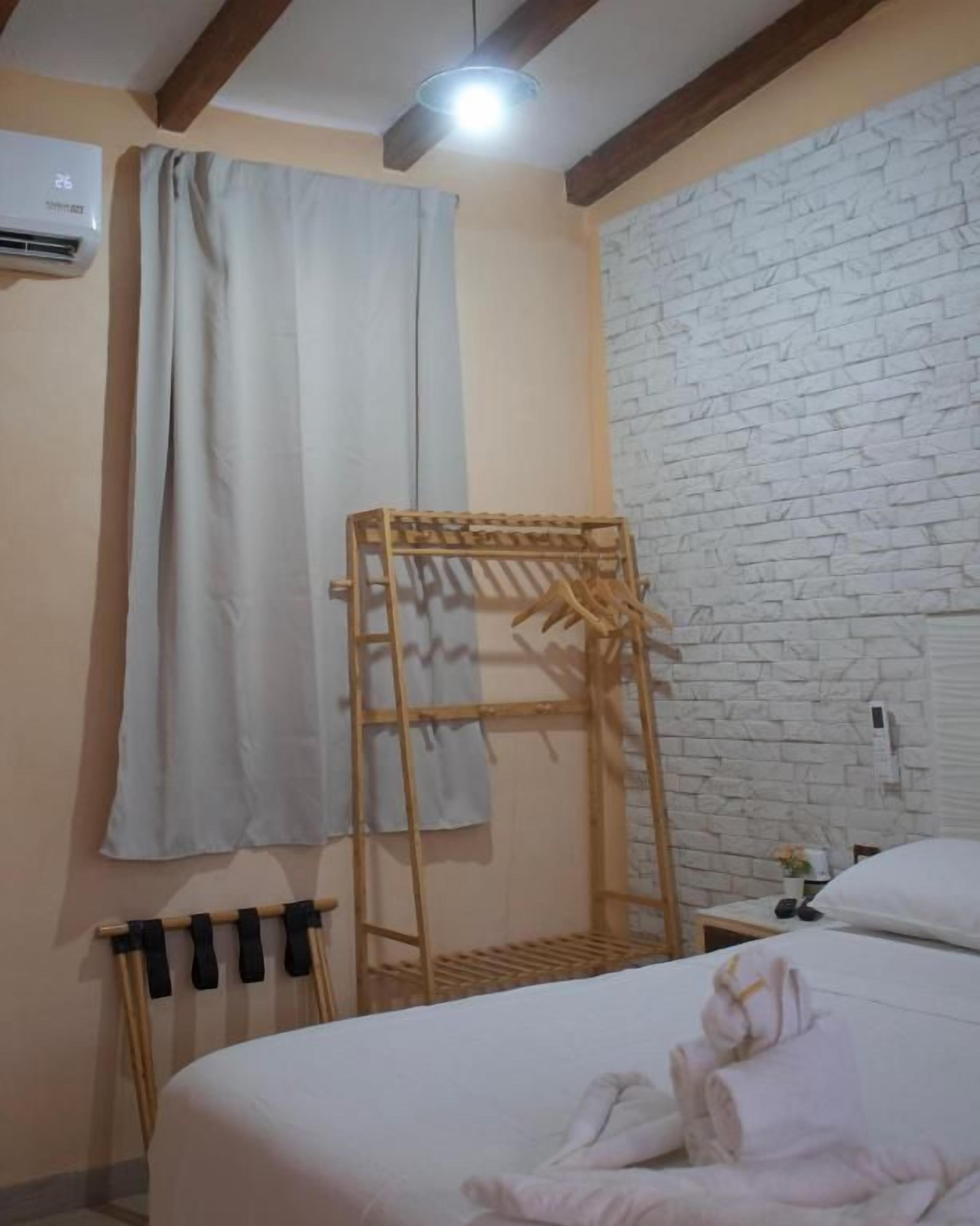 Une chambre à coucher avec un lit, un étendoir en bois, un climatiseur fixé au mur et un mur en briques blanches.