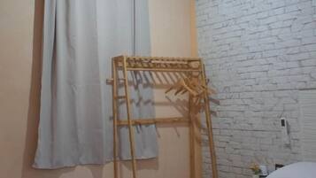 Une chambre à coucher avec un lit, un étendoir en bois, un climatiseur fixé au mur et un mur en briques blanches.