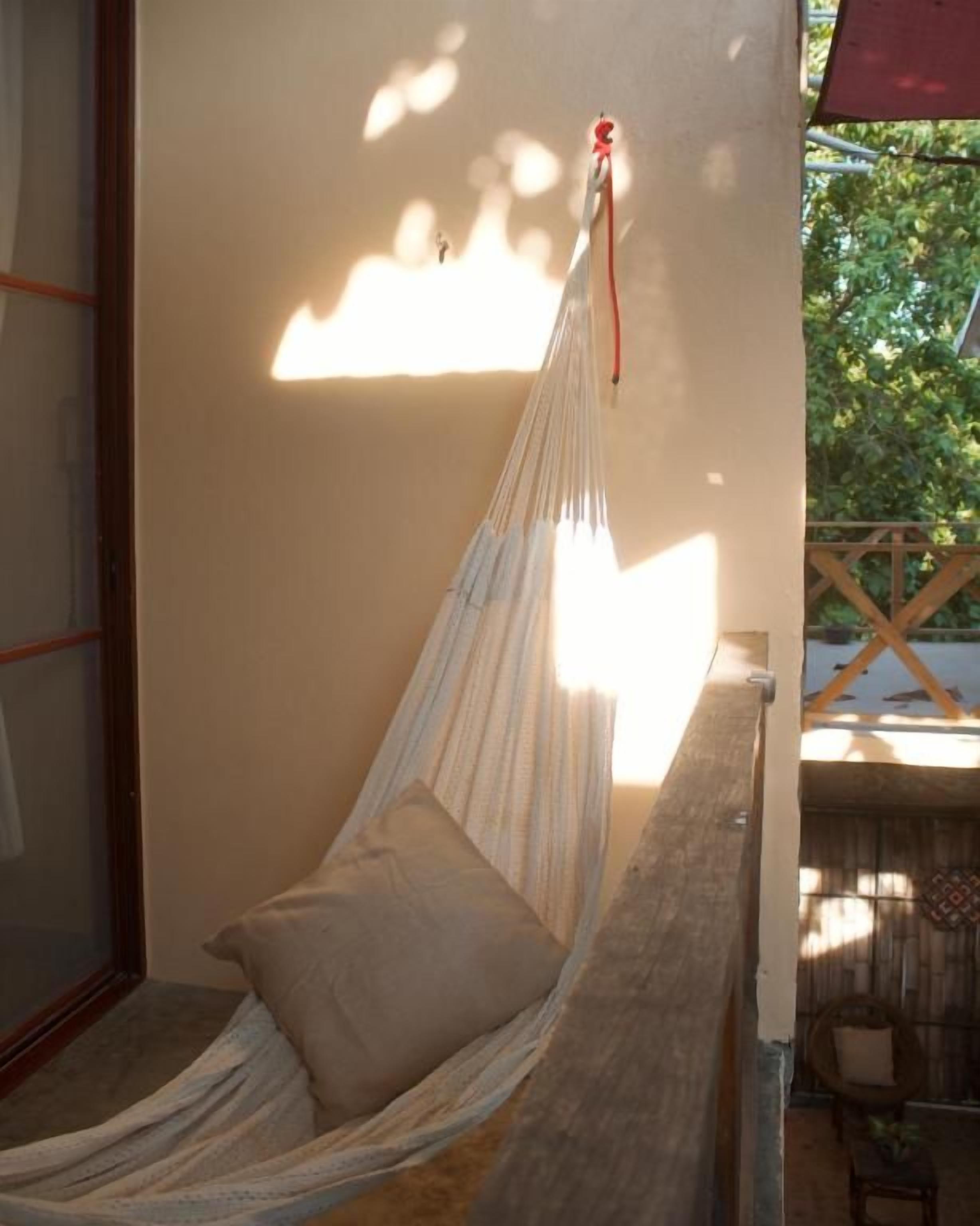 Silla hamaca con cojín, sujeta a una estructura de madera, en una habitación con vistas al verdor exterior.