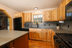 Une cuisine avec des meubles de rangement en bois, un réfrigérateur noir, un four à micro-ondes, un évier et une cuisinière.