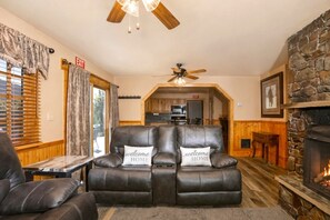 A cozy living room with a fireplace, leather sofa, and a dining area in the background.
