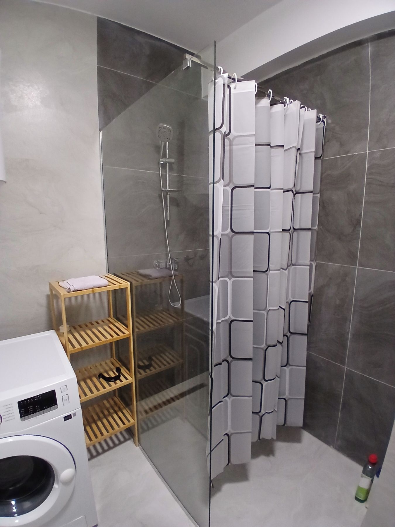 Een moderne badkamer met een douchecabine van glas, een houten plankunit en een witte wasmachine.