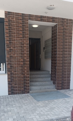 A building entrance with a brick facade, a set of steps leading to a door, and a small outdoor area with a paved surface. - 2-bedroom apartment "Your Home away from Home" (Gostivar)