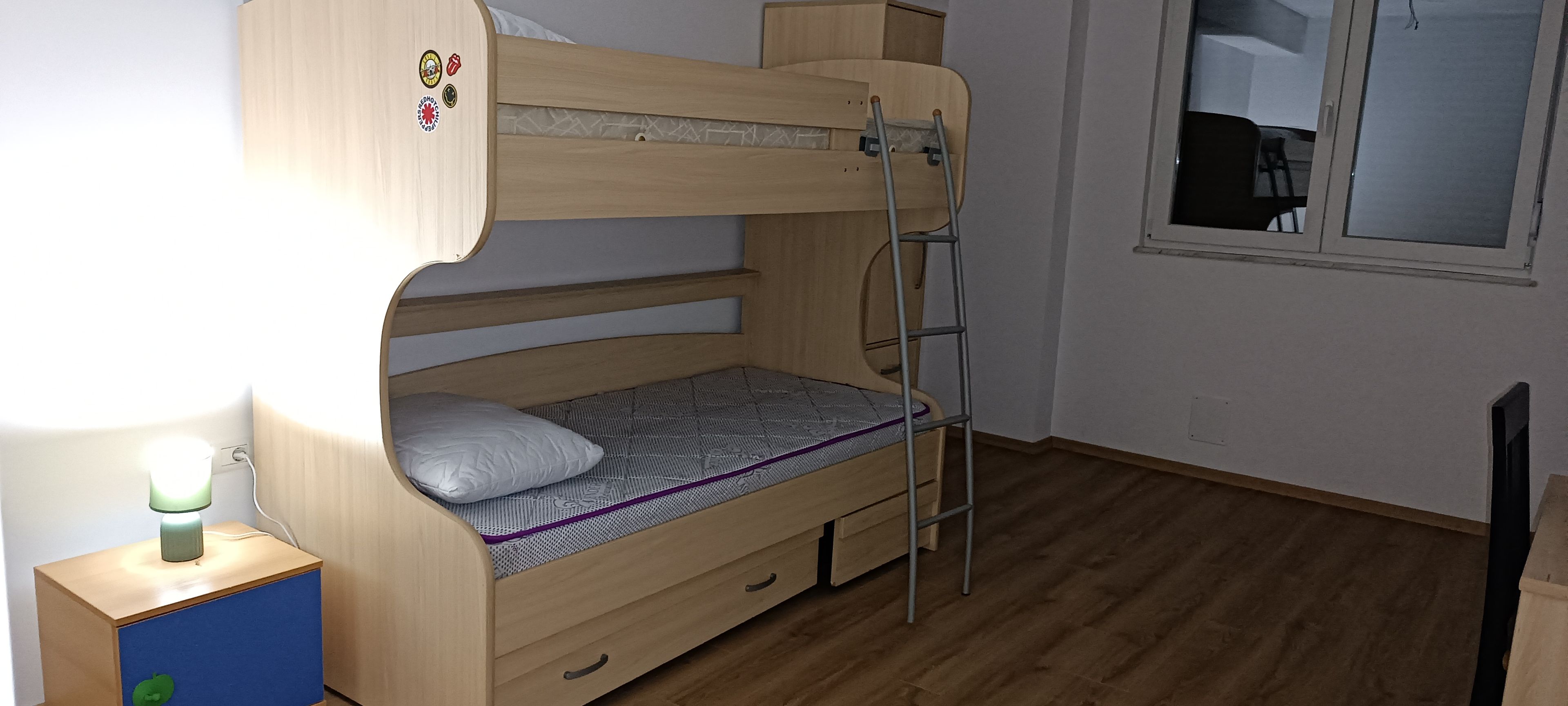 Un lit superposé avec une échelle, une table de chevet avec une lampe et une fenêtre dans la pièce.