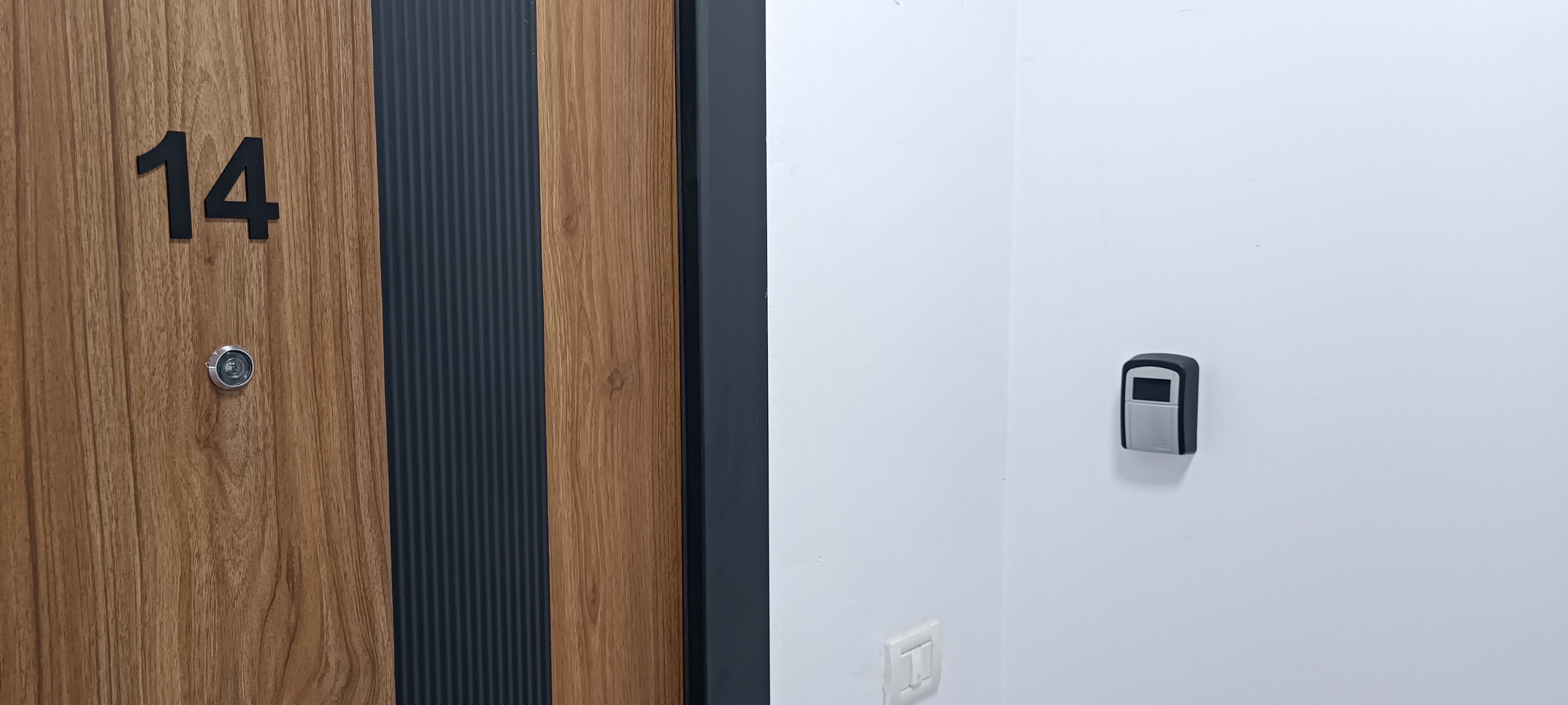 Une porte en bois portant le numéro 14 et munie d’un trou de serrure, un panneau à rayures verticales et un mur blanc avec une poignée de porte.